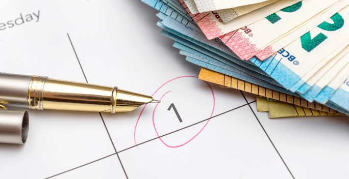 Im Vordergrund ist ein Kalender mit einer eingekreisten eins. Daneben liegen Geldschein.