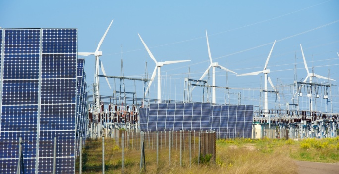 Mehrere Windräder, PV-Module und ein Umspannwerk stehen auf einem Feld und erzeugen Strom.