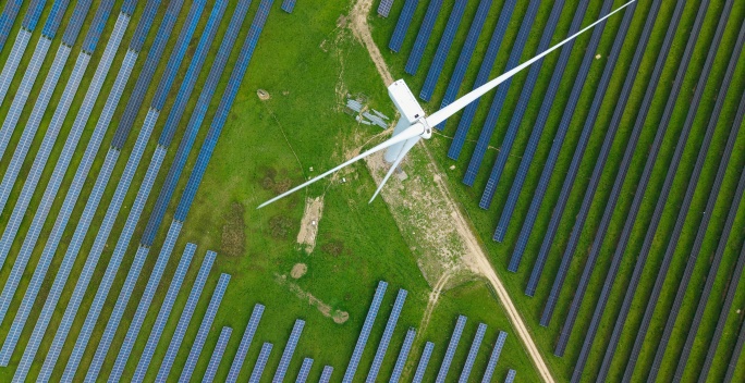 Windrad von oben von einer Drohne aus fotografiert. Um den Windpark befindet sich ein Solarpark