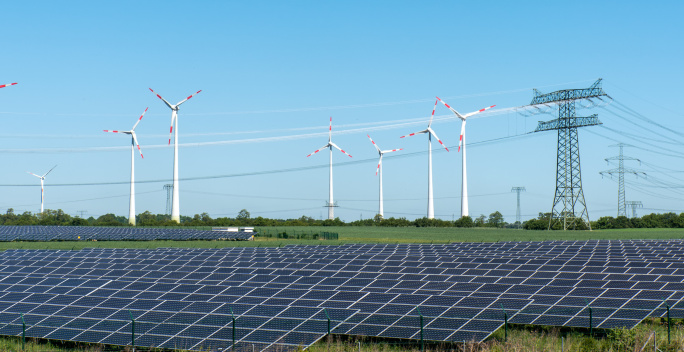 Windenergieanlagen und Solarmodule sind mit Hochspannungsmasten verbunden und speisen Strom in das Netz ein.