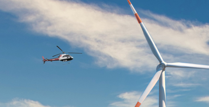 Neben einem Windrad fliegt ein Hubschrauber im Luftraum.