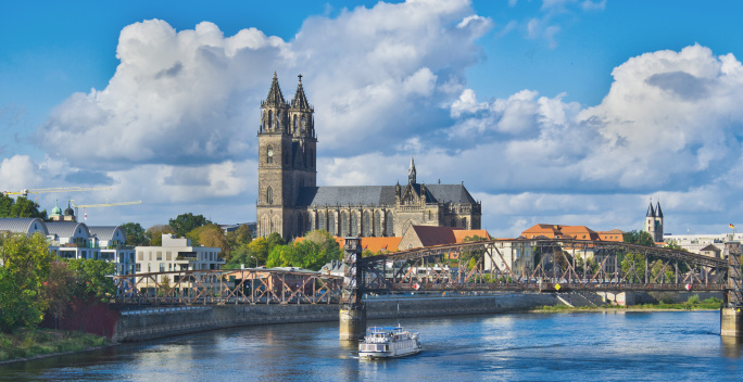 Auf dem Bild befindet sich im Vordergrund die Elbe mit einer Brücke. Im Hintergrund befindet sich der Dom zu Magdeburg