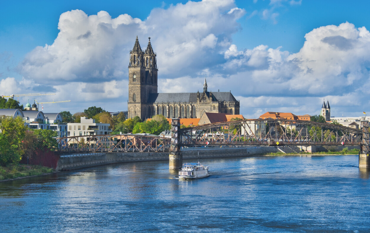 Auf dem Bild befindet sich im Vordergrund die Elbe mit einer Brücke. Im Hintergrund befindet sich der Dom zu Magdeburg