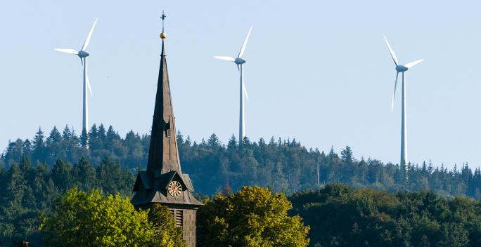 Auf diesem Bild sind Windkraftanlagen und ein Kirchturm zu erkennen.