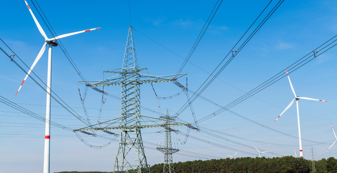 Das Bild zeigt mehrere Windräder mit rot-weißen Markierungen sowie Hochspannungsleitungen.