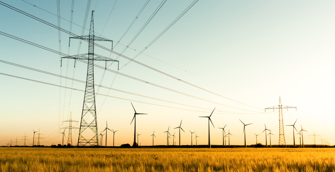 Um einen Windpark stehen mehrere Freileitungsmasten.