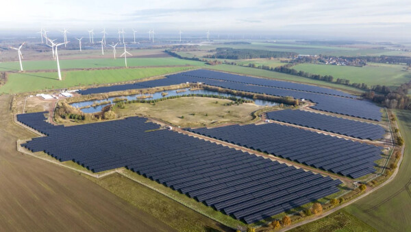 Drohnenaufnahme vom Solarpark in Zerbst mit Windenergieanlagen im Hintergrund.